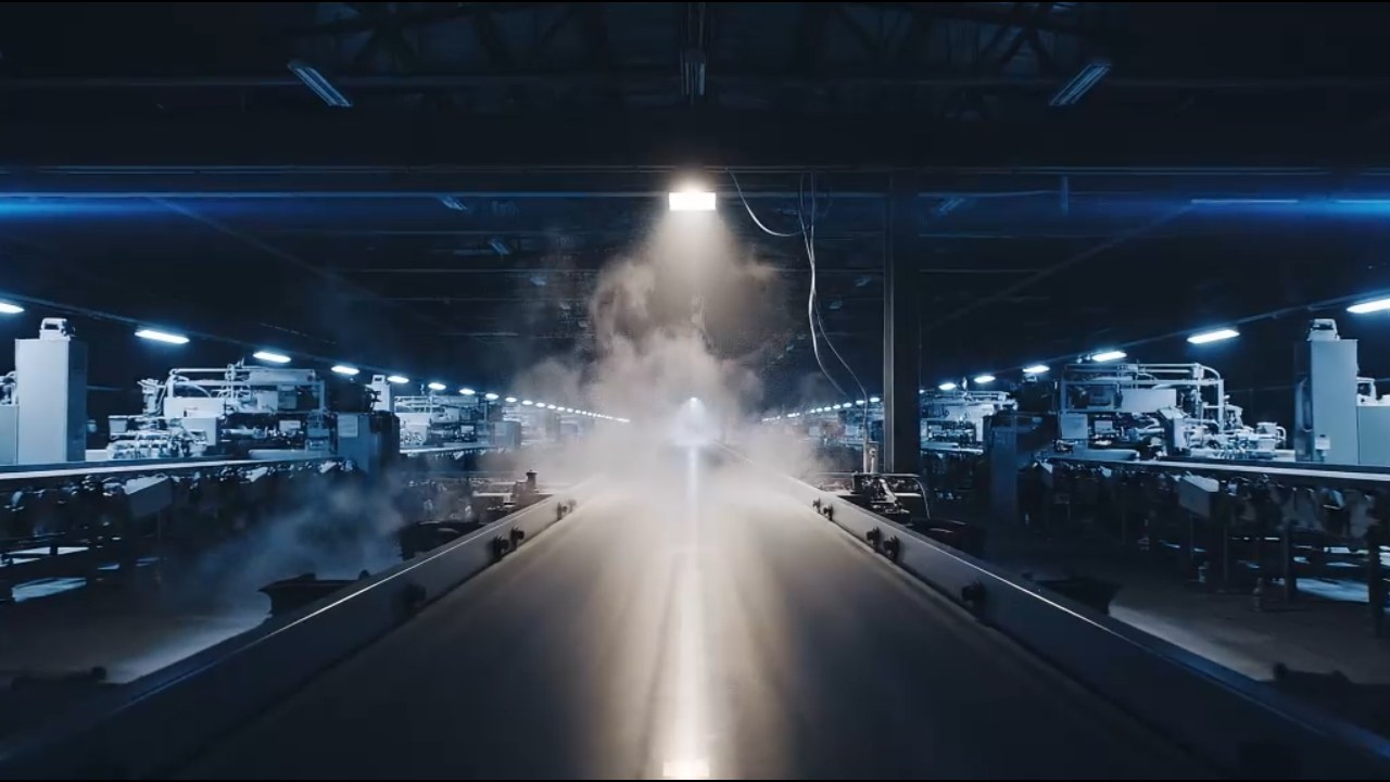 A dark automated sortation facility at night, a worklight beam cutting through steam above a conveyor line.